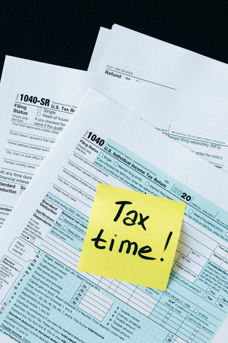 A-pile-of-U.S.-tax-documents-including-Form-1040-with-a-bright-yellow-sticky-note-reading-'Tax-time!'-on-top,-emphasizing-tax-preparation.